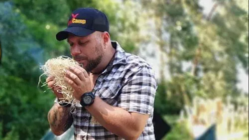 Man wearing a cap holds straw outdoors.