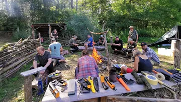 Group sitting around campfire in wooded area.