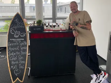 Cocktailbar mit Barkeeper, der freudig posiert.