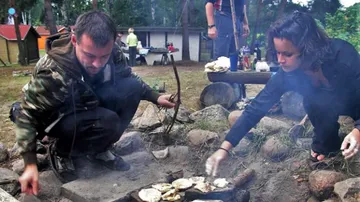 Zwei Personen kochen am Lagerfeuer im Wald.