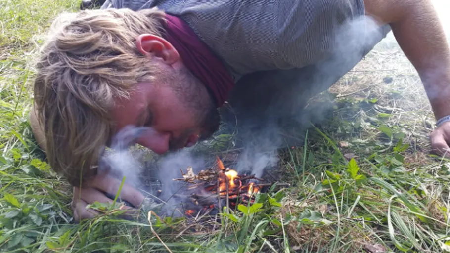 Person blows on small campfire in grassy field.