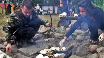Zwei Personen kochen am steinernen Außenfeuer.
