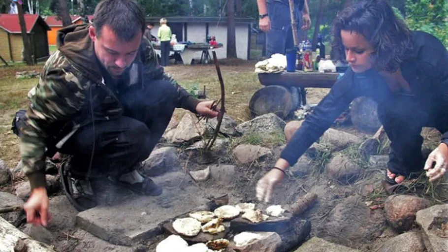 Two people cook over outdoor stone fire pit.