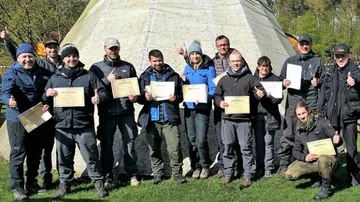 Gruppe von Menschen hält Zertifikate vor Zelt.
