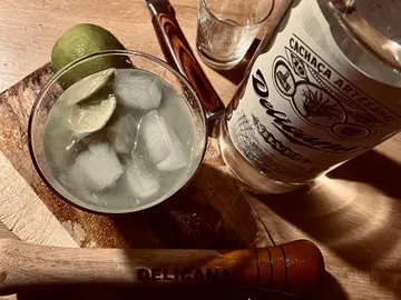 Cocktailglas mit Eis, Limette und Cachaca auf Holzunterlage.