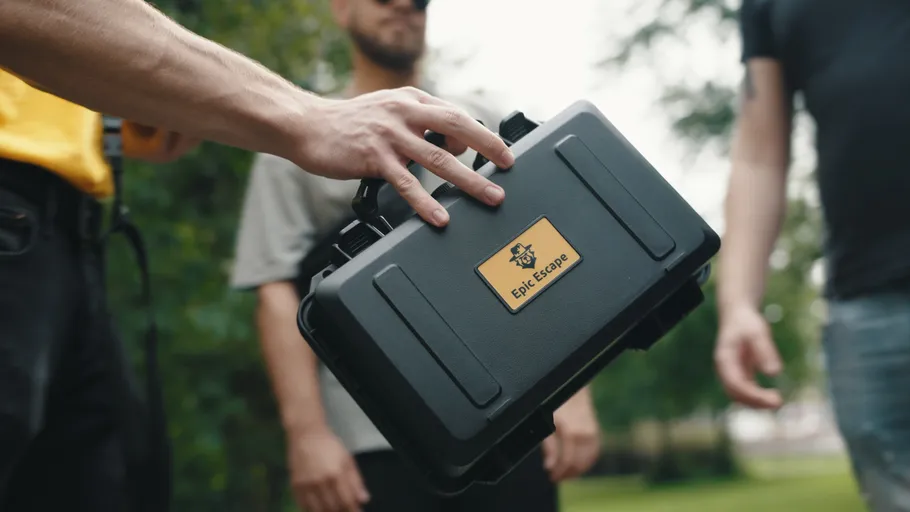 Hand hält schwarzen Koffer im Freien mit Personen nahbei.