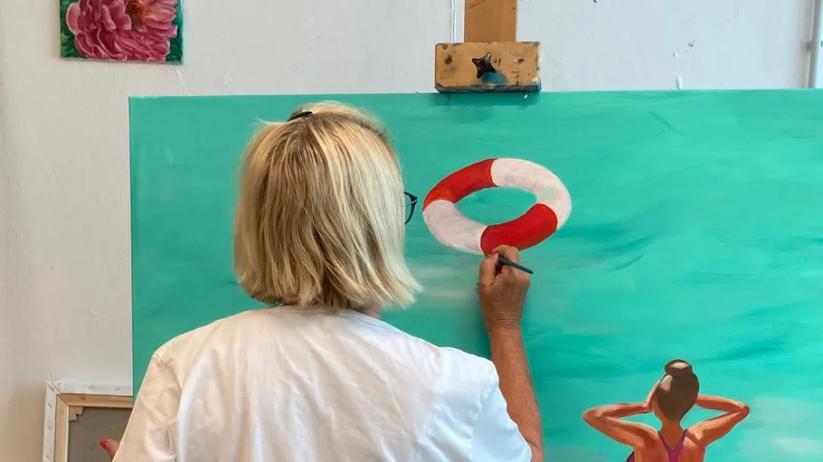 Woman painting lifesaver on ocean-themed canvas.