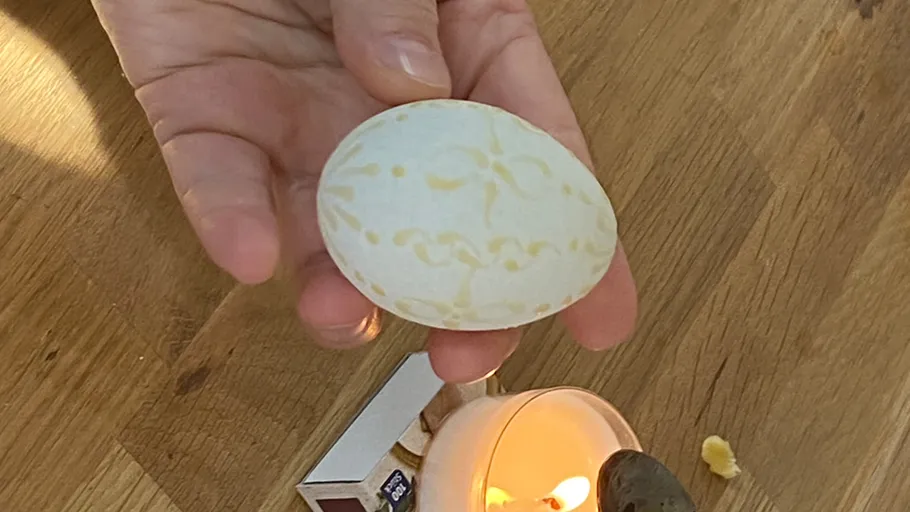 Hand hält verziertes Ei über Kerze.