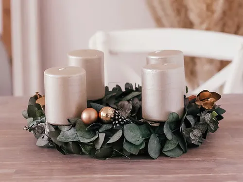 Candles stand on a wreath of eucalyptus leaves.