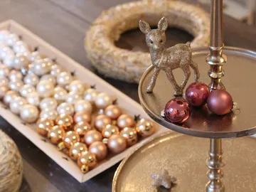 Glitzerndes Reh steht neben Weihnachtskugeln auf Tischdeko.