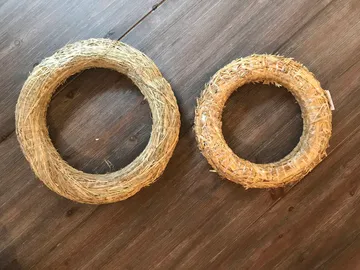 Zwei Strohkränze liegen auf einem Holztisch.