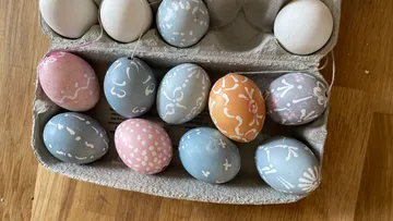 Decorated eggs in a carton on wooden table.