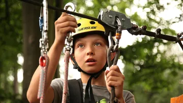Junge mit Helm benutzt Seilrutschenausrüstung im Freien.