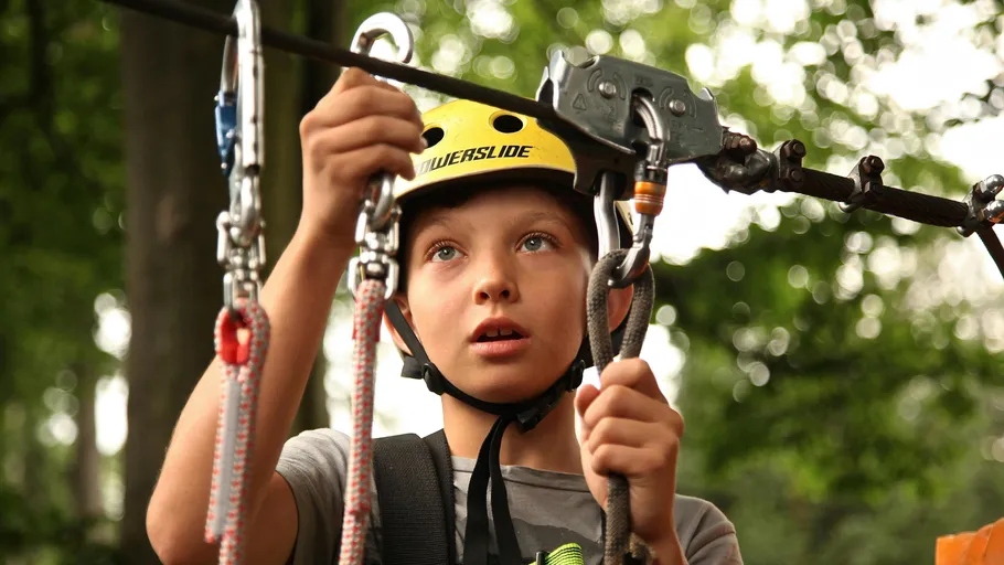Boy wearing helmet using zip line equipment outdoors.