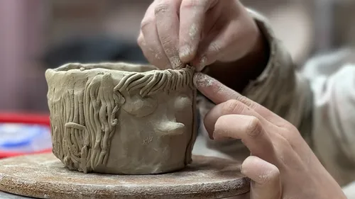 Hands shaping clay pot on wheel.