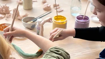 Kinder bemalen Tonfiguren am Tisch.