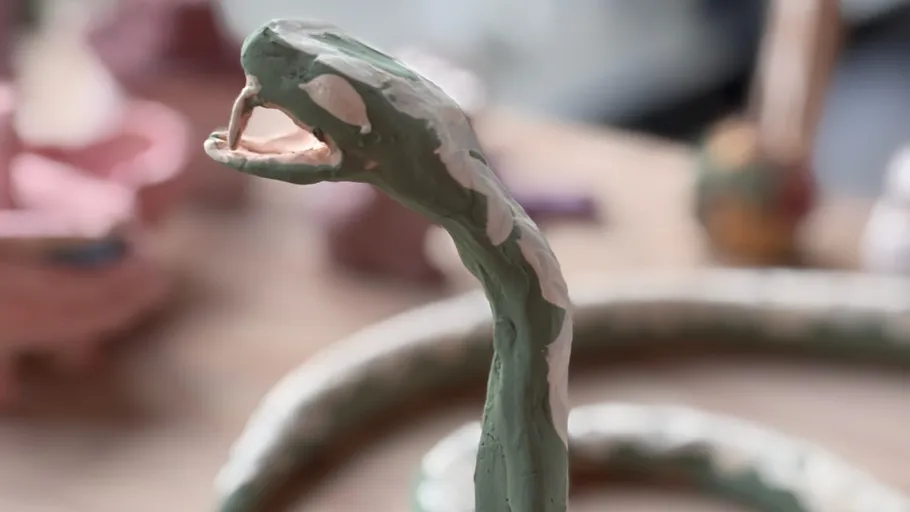 Clay snake sculpture with open mouth indoors.
