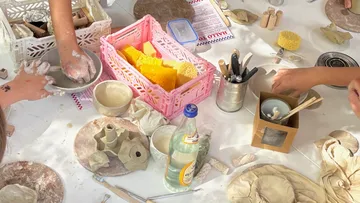 Hands crafting ceramics on a cluttered table.