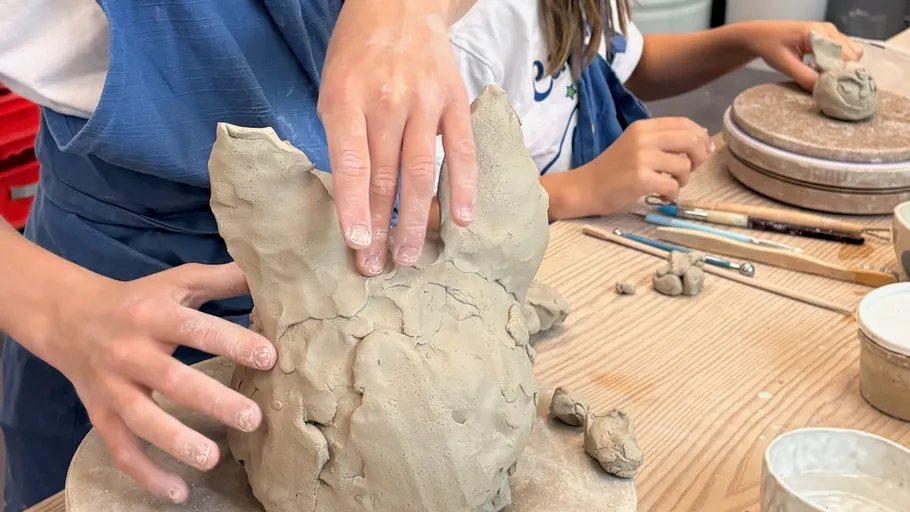 Child shaping clay animal figure on table.
