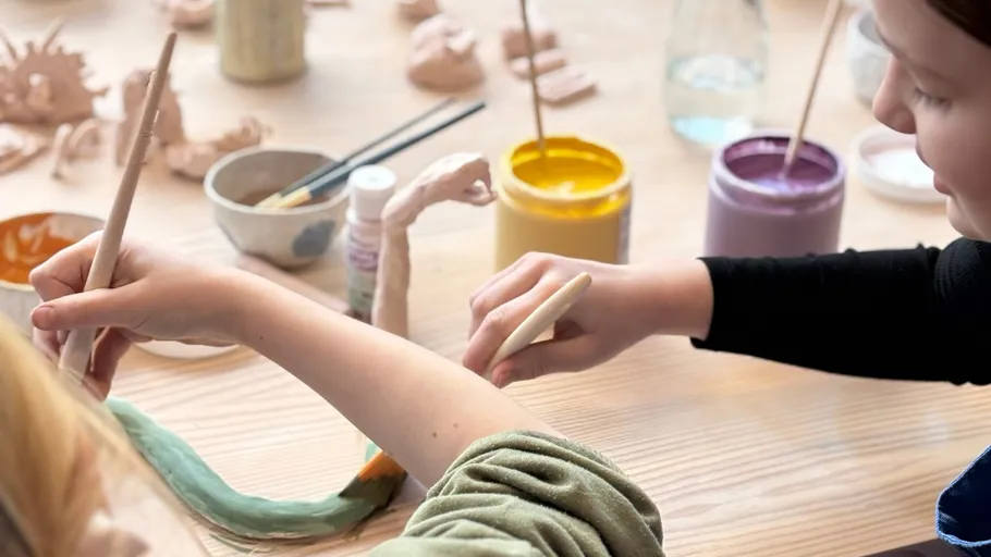 Children painting clay sculptures on a table.