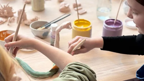 Children painting clay sculptures at a table.