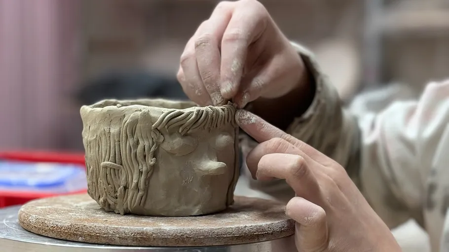 Hands sculpting clay pot in studio.
