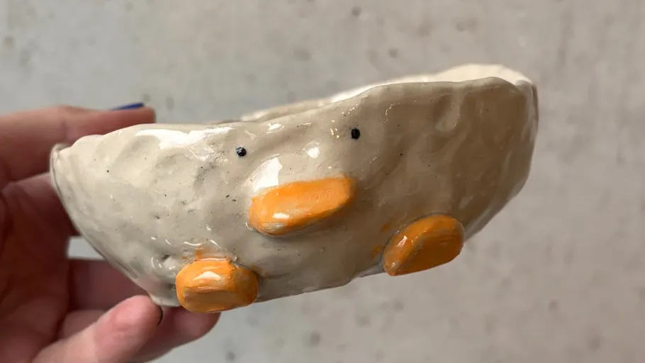 Ceramic bowl shaped like a duck, hand holding.