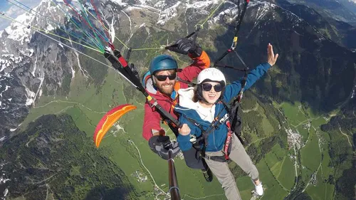 Zwei Personen beim Paragliding über Berglandschaft.