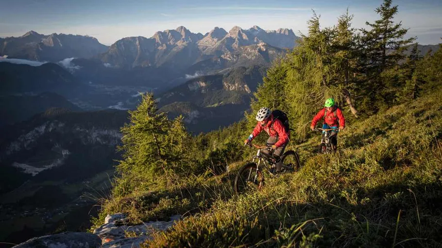 Two cyclists riding mountain trail at sunrise.