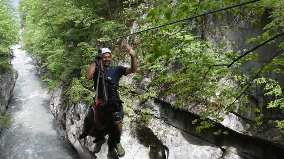 Man ziplining with goat over a gorge.