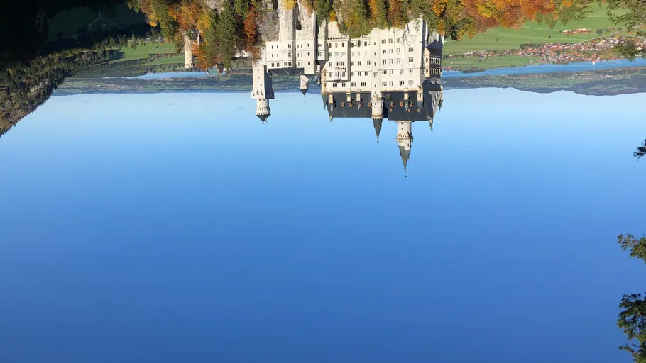 Schloss mit Türmen in bewaldeter Landschaft.