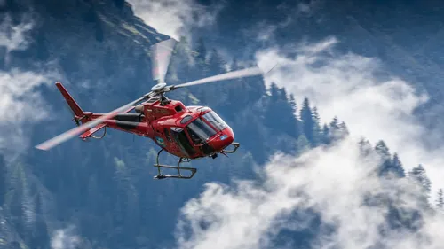 Roter Hubschrauber fliegt über gebirgiges Gelände.