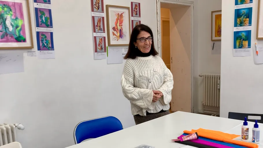 Frau lächelt in kunstvollem Raum, trägt Pullover.