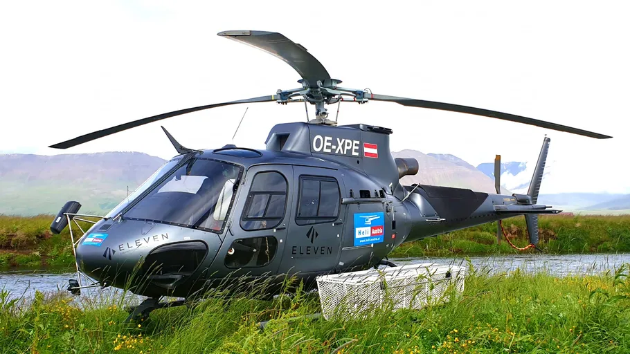 Hubschrauber parkt auf Wiese, Bergkulisse im Hintergrund.
