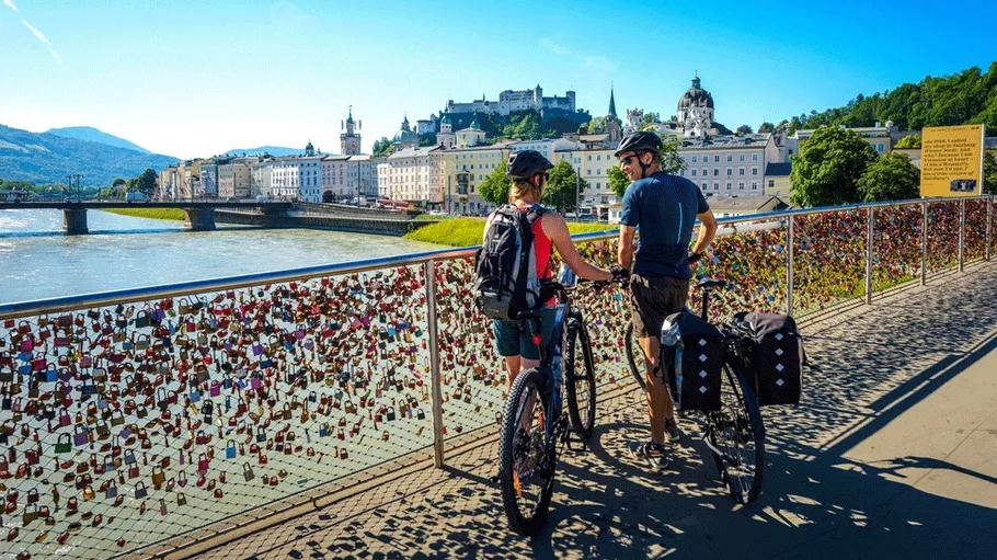 Two cyclists admire the Salzburg cityscape from a bridge.