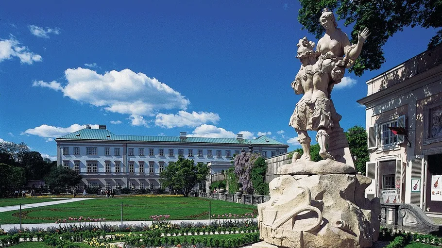 Statue in garden with historical building backdrop.