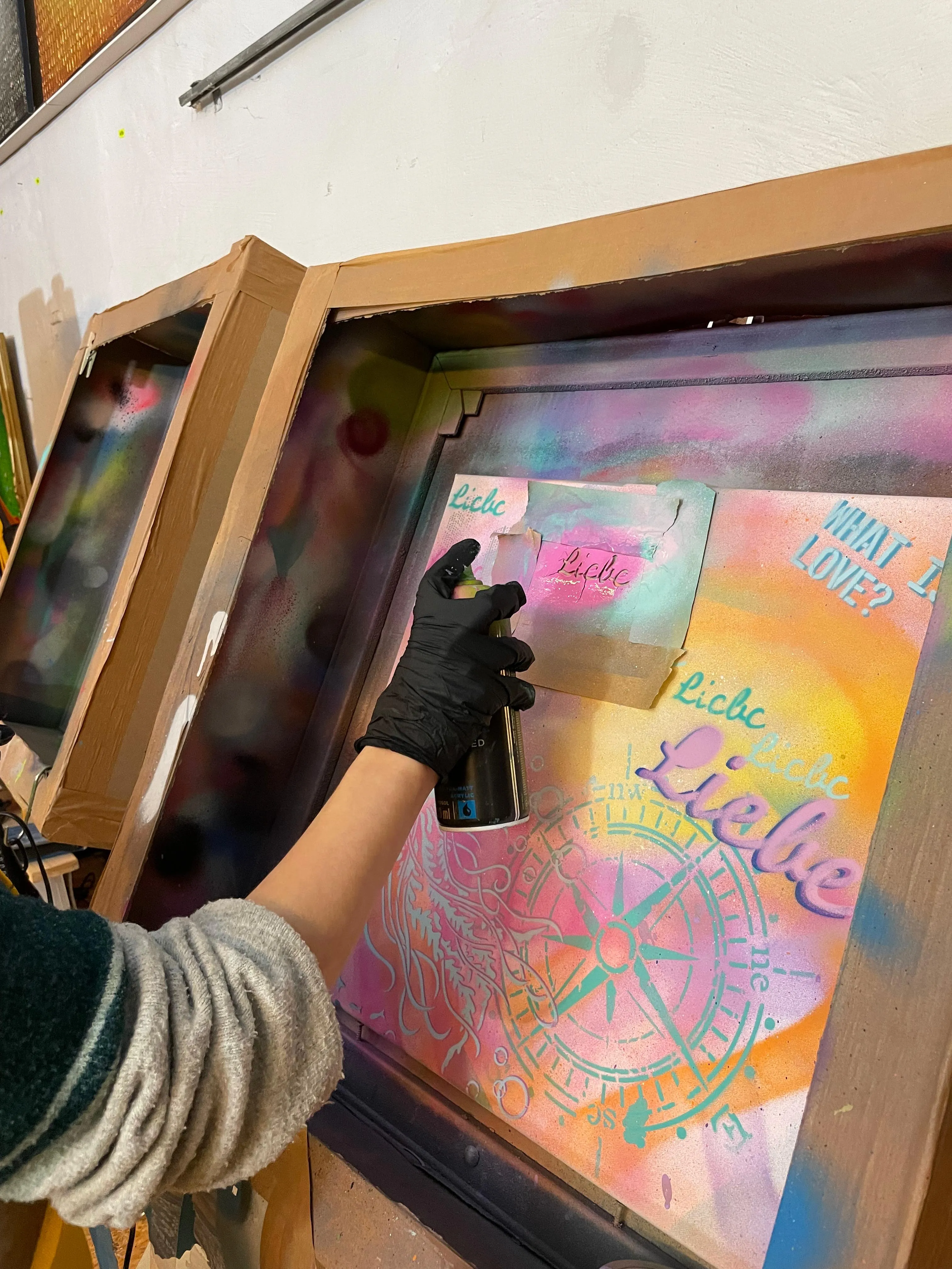 Person sprayt buntes Kunstwerk auf Karton.