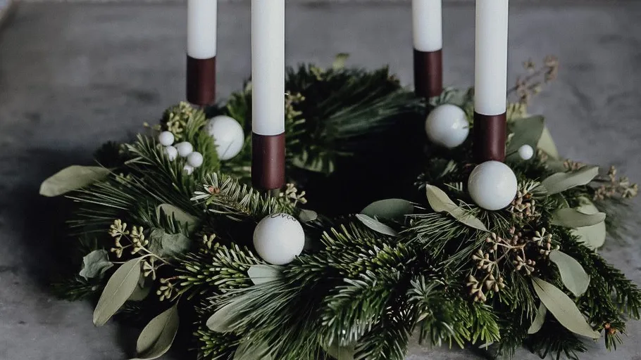 Green wreath with white candles on table.