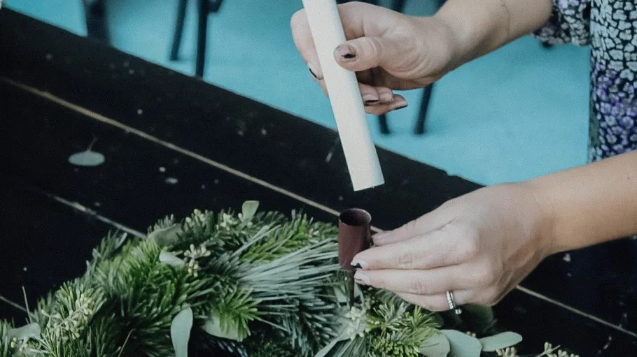 Person assembling candle on a Christmas wreath.