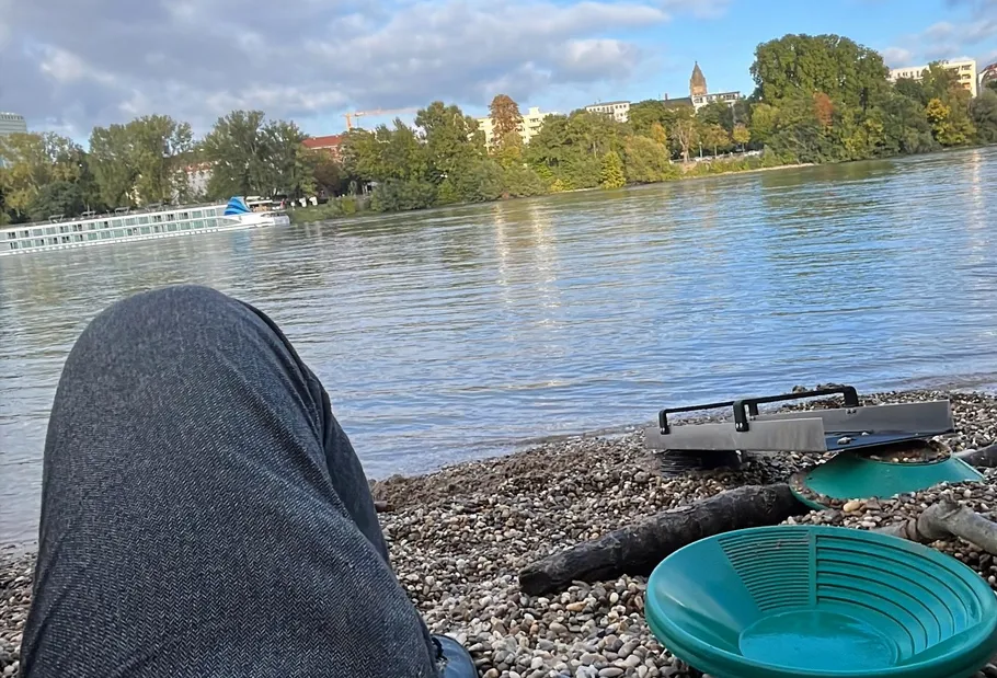 Person relaxing by river, cityscape in background.