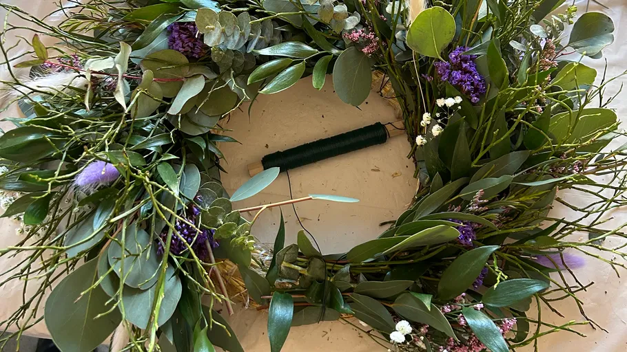 Wreath-making with green leaves on table.