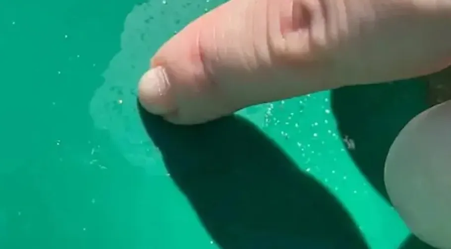 Finger touching reflective green surface.