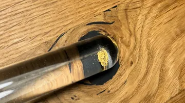 Reagenzglas mit gelber Substanz auf Holzoberfläche.