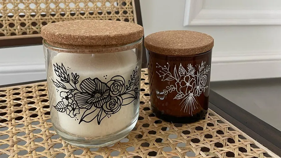 Two floral-decorated candles on woven chair.