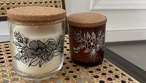 Two decorative candles with floral designs, cork lids.