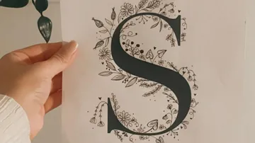 Hand holding paper with decorative letter S.