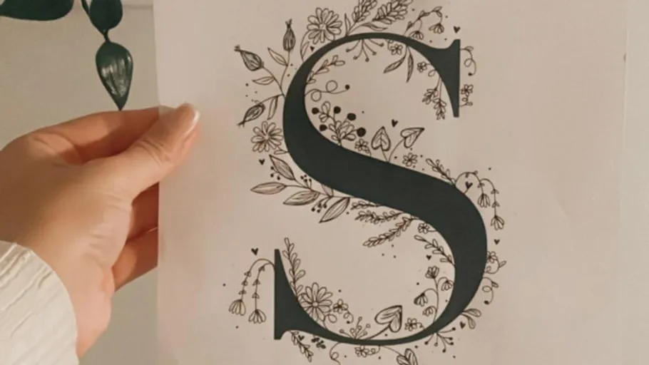 Hand holding paper with decorative letter S.