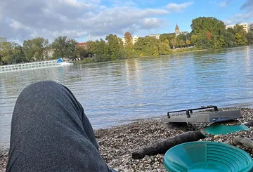 Person entspannt am Flussufer mit Pfannen daneben.
