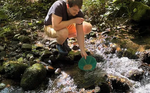 Man pans for gold in rocky stream.