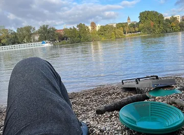 Person sitting by the riverside with equipment.